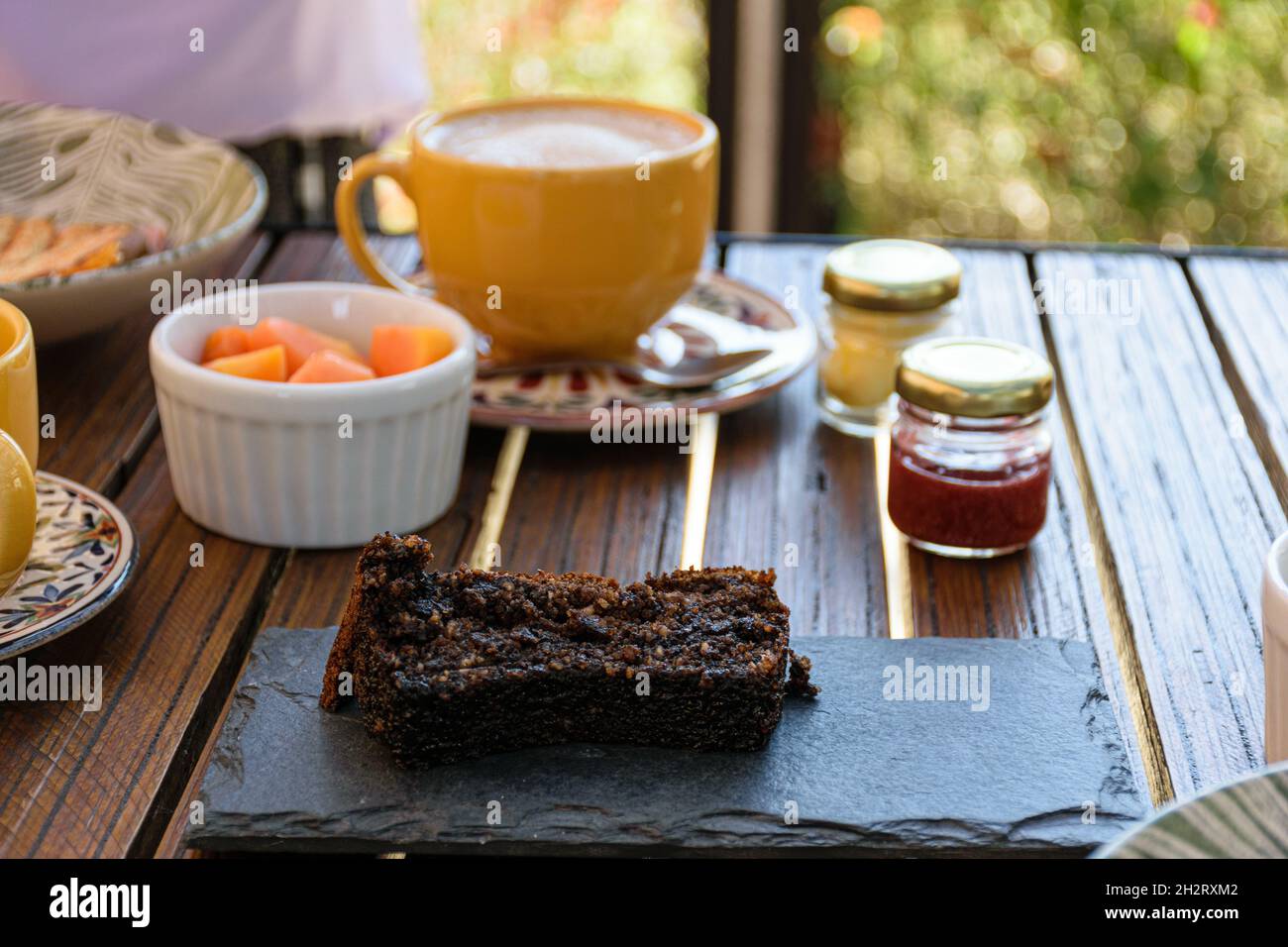 Kekskuchen auf einem Schieferbrett, neben verschiedenen Marmeladen, Papaya und einer Tasse Latte. Stockfoto