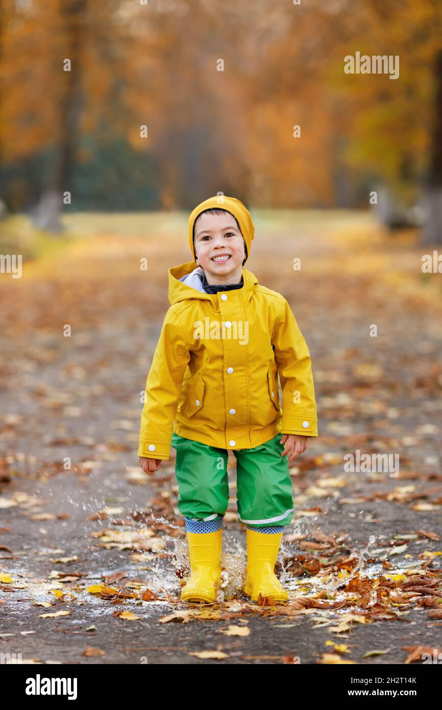 Fröhlicher Junge mit gelbem Regenmantel, der in der Pfütze springt Stockfoto
