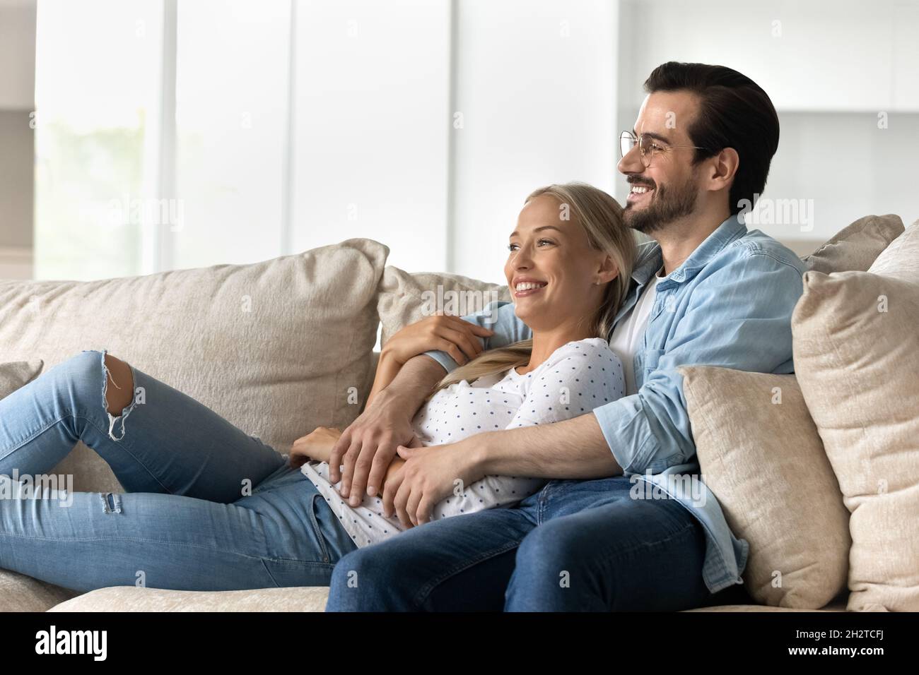 Glückliches Bonden verträumtes junges Familienpaar, das sich auf einem gemütlichen Sofa ausruht. Stockfoto