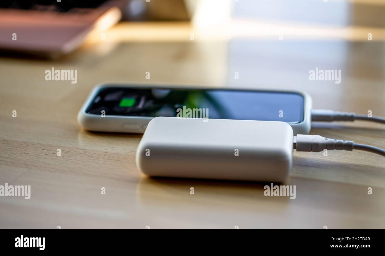 Ein Smartphone wird von einer kleinen weißen Powerbank geladen. Stockfoto