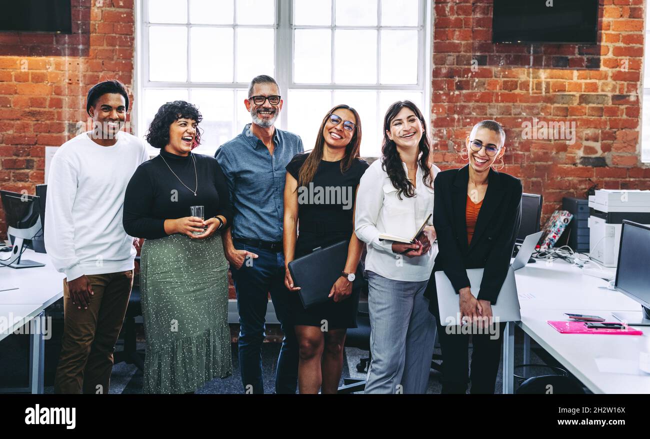 Erfolgreiche Geschäftsleute lächeln fröhlich in einem Büro. Gruppe glücklicher Geschäftsleute, die gemeinsam an einem kreativen Arbeitsplatz stehen. Geschäftskollege Stockfoto