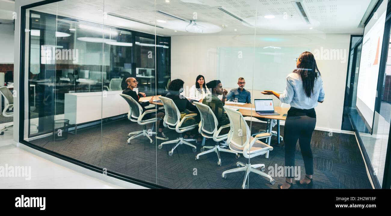 Kreative Geschäftsfrau, die eine Präsentation in einem Sitzungssaal gibt. Selbstbewusste Geschäftsfrau, die ihren Kollegen Finanzdaten an einem modernen Arbeitsplatz präsentiert Stockfoto