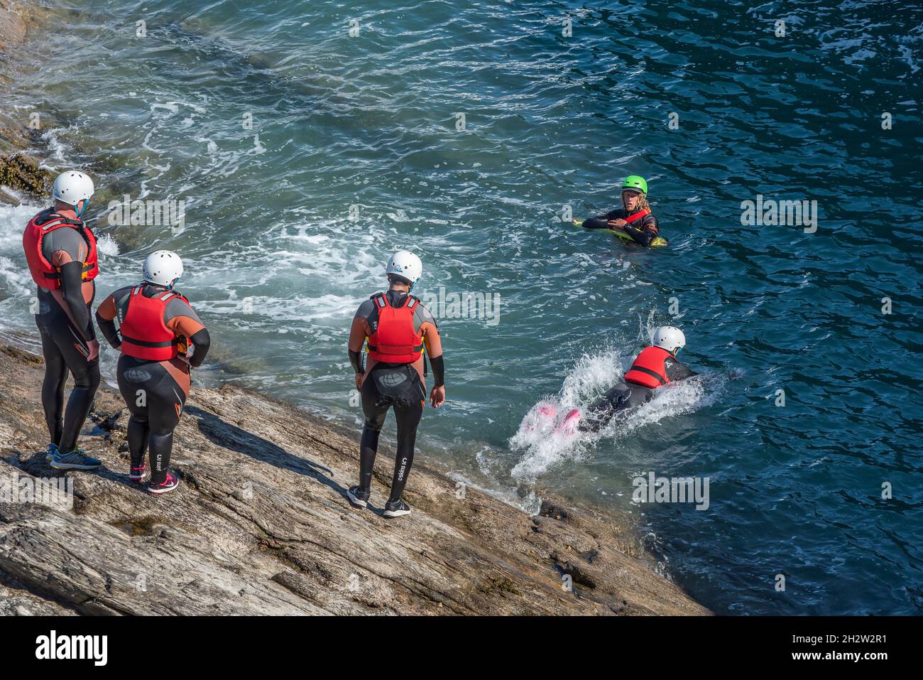 Urlauber und ihr Coasteering Guide an der Küste von Towan Head in Newquay in Cornwall. Stockfoto