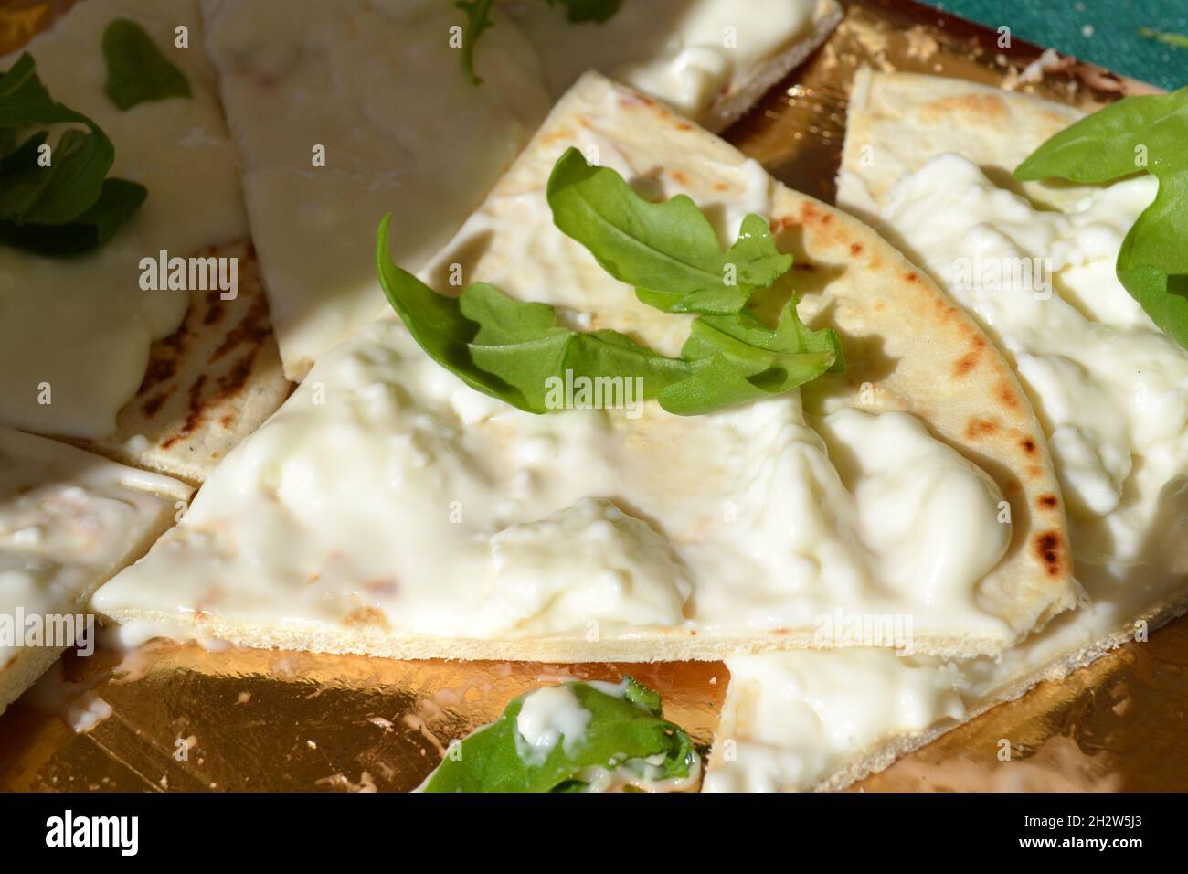 Focaccia-Stück mit weichem Weißkäse übertännt und mit Rocket Salad verziert, der auf dem goldenen Tablett unter der strahlenden Sonne platziert wurde. Italienisches Essen. Nahaufnahme Stockfoto