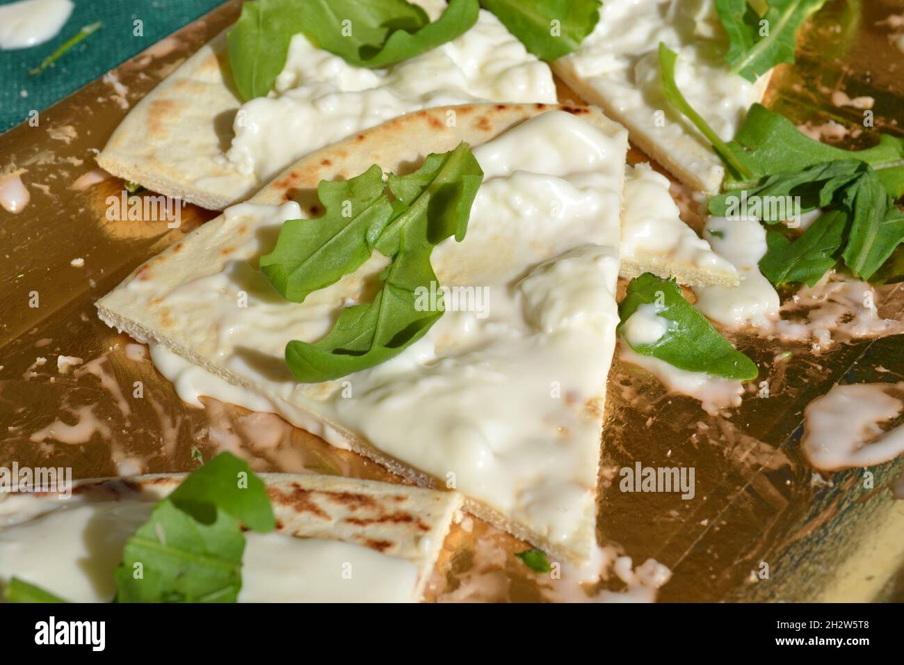 Focaccia-Stück mit weichem Weißkäse übertännt und mit Rocket Salad verziert, der auf dem goldenen Tablett unter der strahlenden Sonne platziert wurde. Italienisches Essen. Nahaufnahme Stockfoto