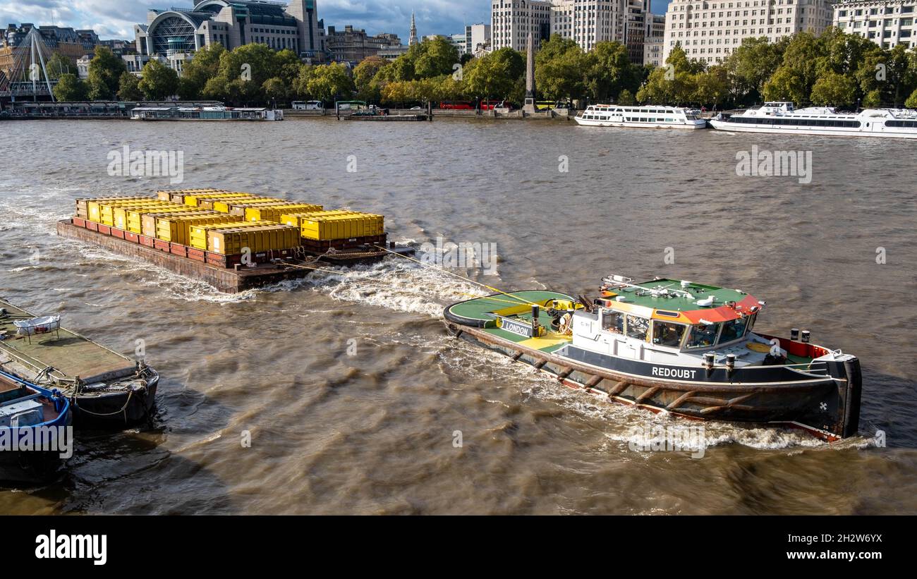 Arbeitsboot oder Schlepper, der einen Brage zieht, der Metallabfallbehälter entlang der Themse in London, England, transportiert Stockfoto