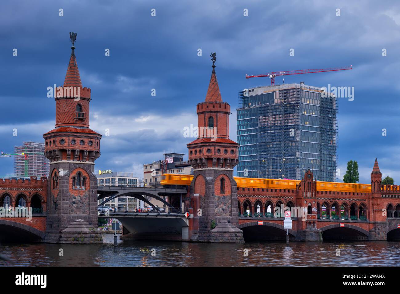 Stadt Berlin in Deutschland, Oberbaumbrücke ab 1895 an der Spree in der Abenddämmerung mit vorbeifahrenden Zug, norddeutsche Backsteingotik mit zwei Türmen Stockfoto