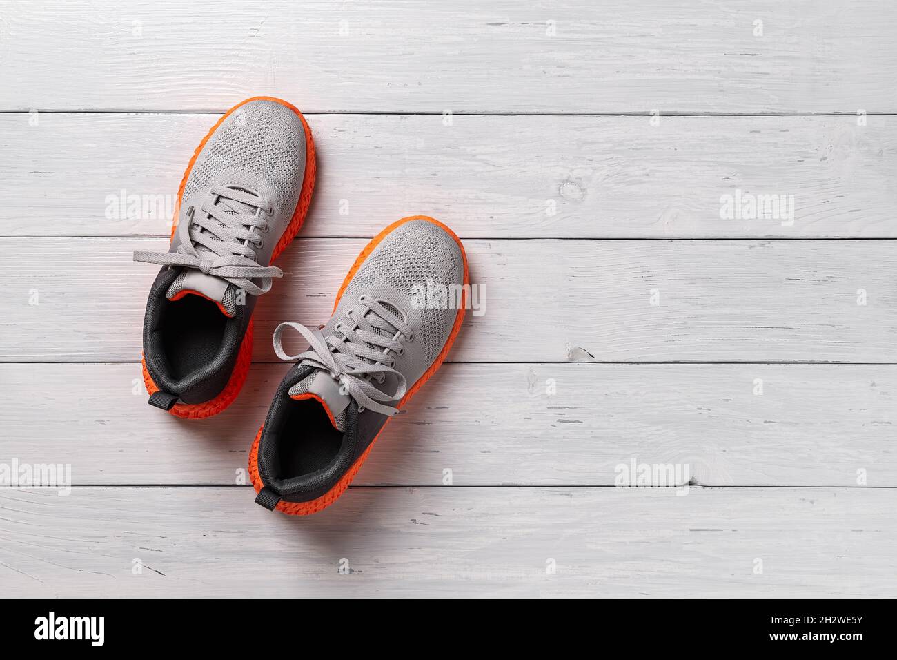 Neu geschnürte Textil-Sneakers auf dem grauen Holzboden. Stylisches Paar Turnschuhe aus Mesh-Material mit gerillter oranger Sohle für aktiven Lifestyle und Fitness Stockfoto