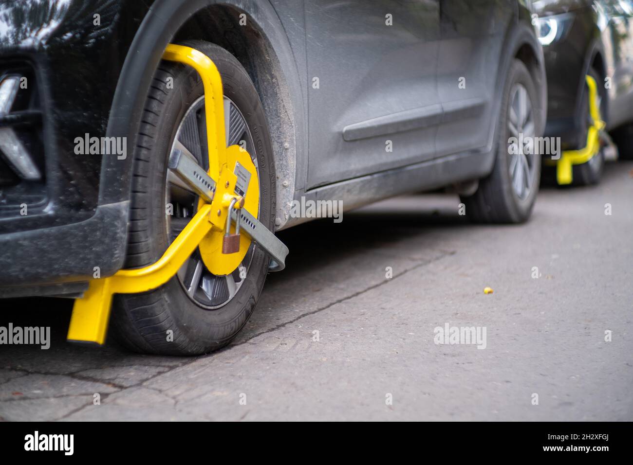 Gelbes Radschloss an einem zufälligem Auto auf der Straße. Verstoß gegen das Parken, gemeinsame Strafe für das Blockieren eines Autos aus dem Verkehr Stockfoto