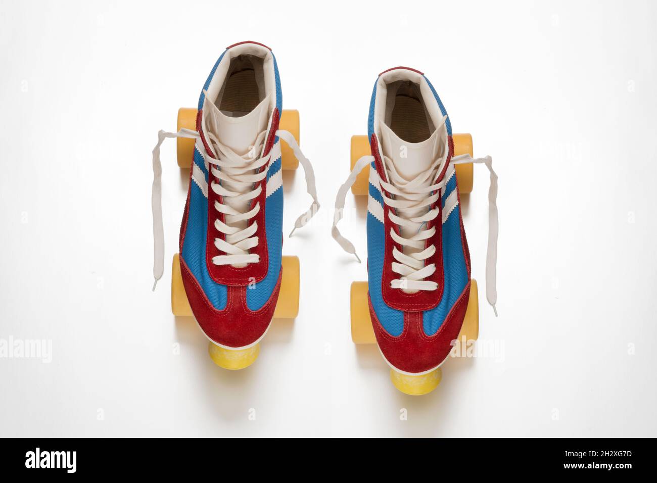 Draufsicht auf ein Paar altmodischer Quadroller-Schlittschuhe mit gelben Rädern und blauen und roten Stiefeln mit Schnürsenkeln auf weißer Oberfläche Stockfoto