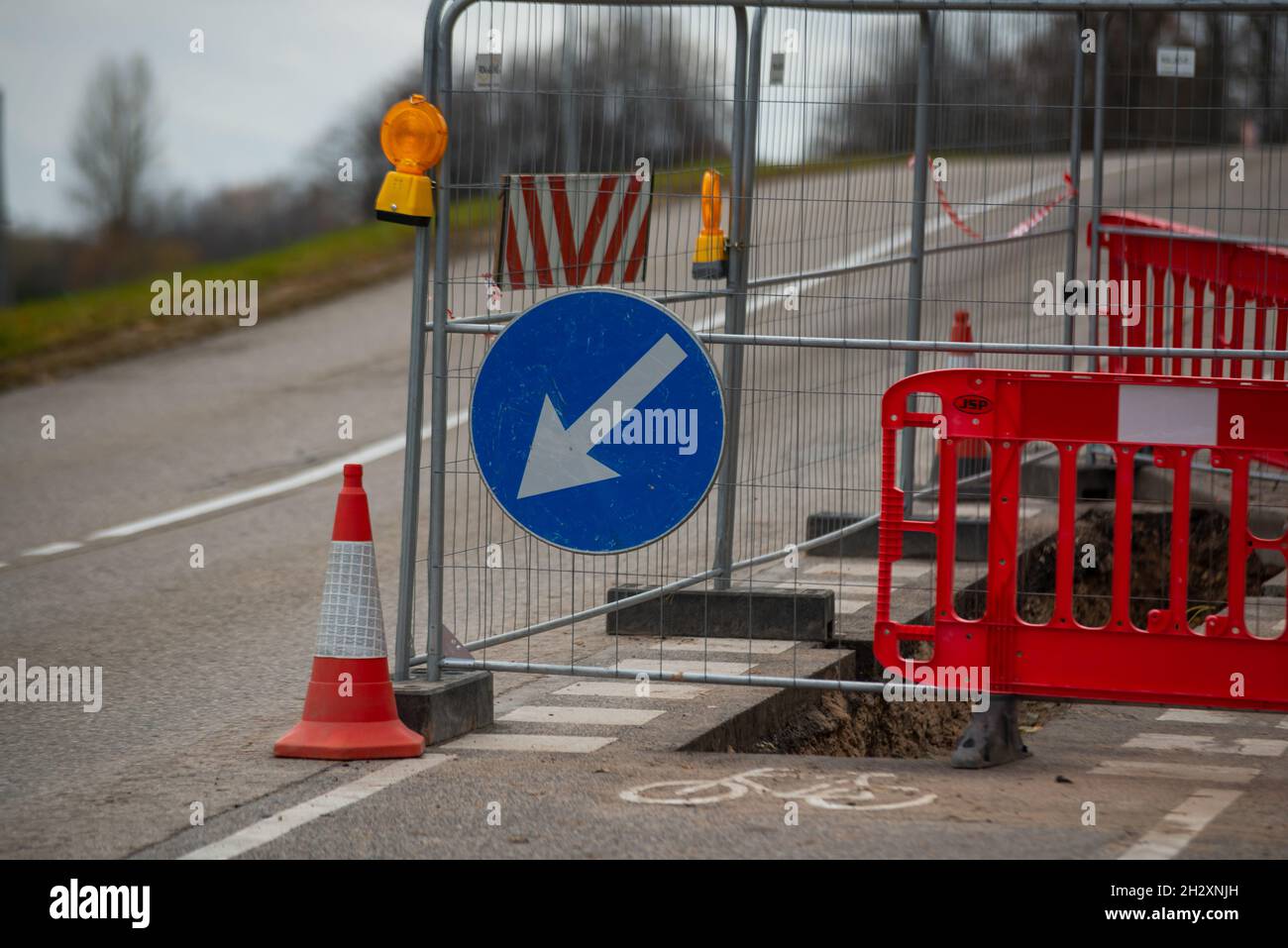 Straßenreparatur auf einer Fahrradspur. Mit einem Zaun begrenzt ausgegrabene Grube während Straßenreparaturen über den Radweg. Bypass-Schild Stockfoto