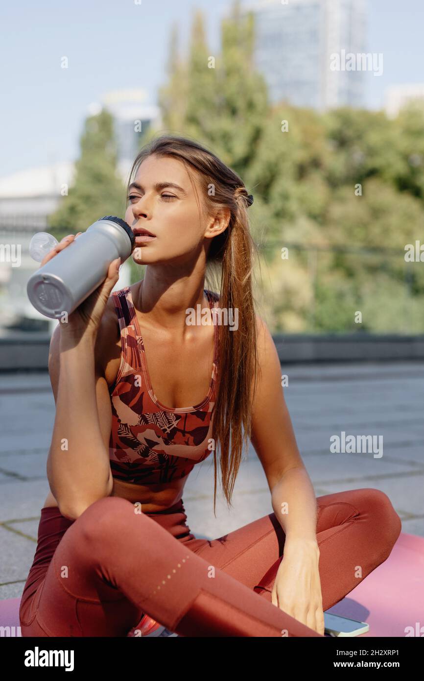 Sportliche junge Frau trinkt nach dem Training draußen Wasser. Stockfoto