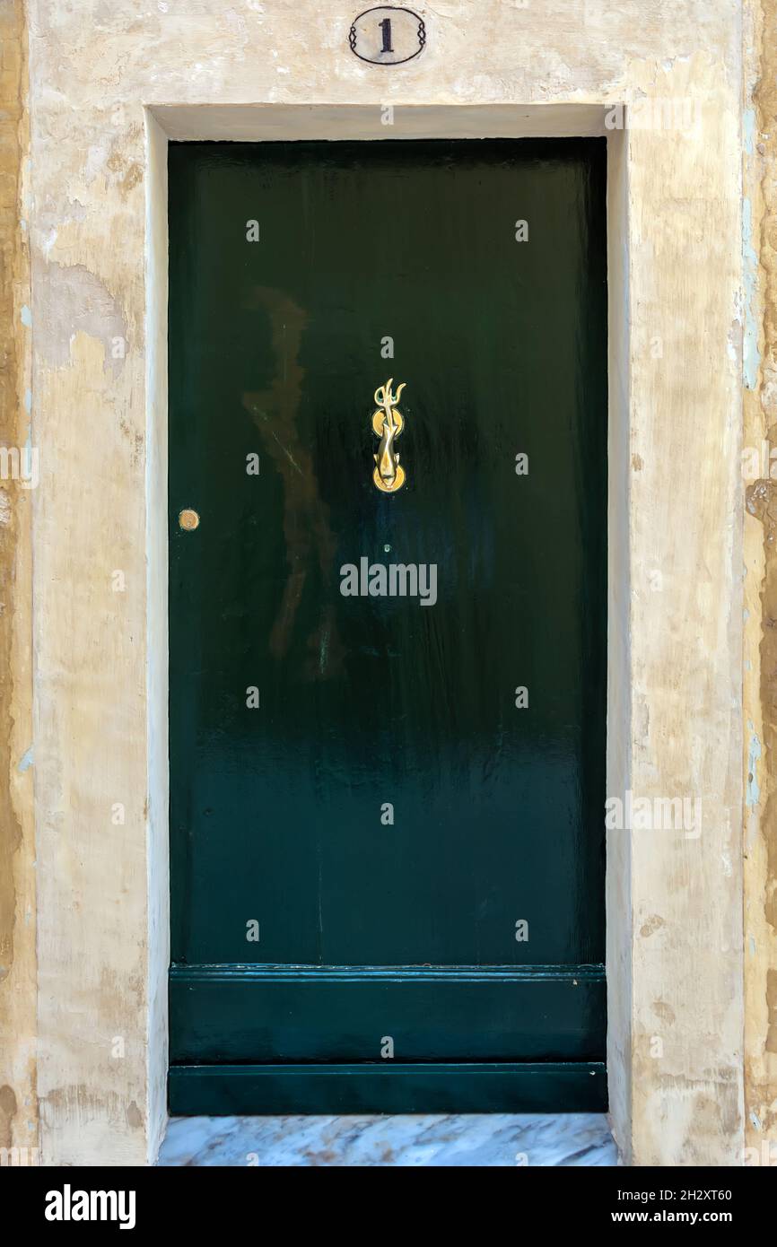 Schwarze Holztür mit Messing Vintage Klopfer als Delphin mit einem dreizackigen Schwanz. Schwarze Tür mit Gusskupferbeschläge mit Patina. Stockfoto