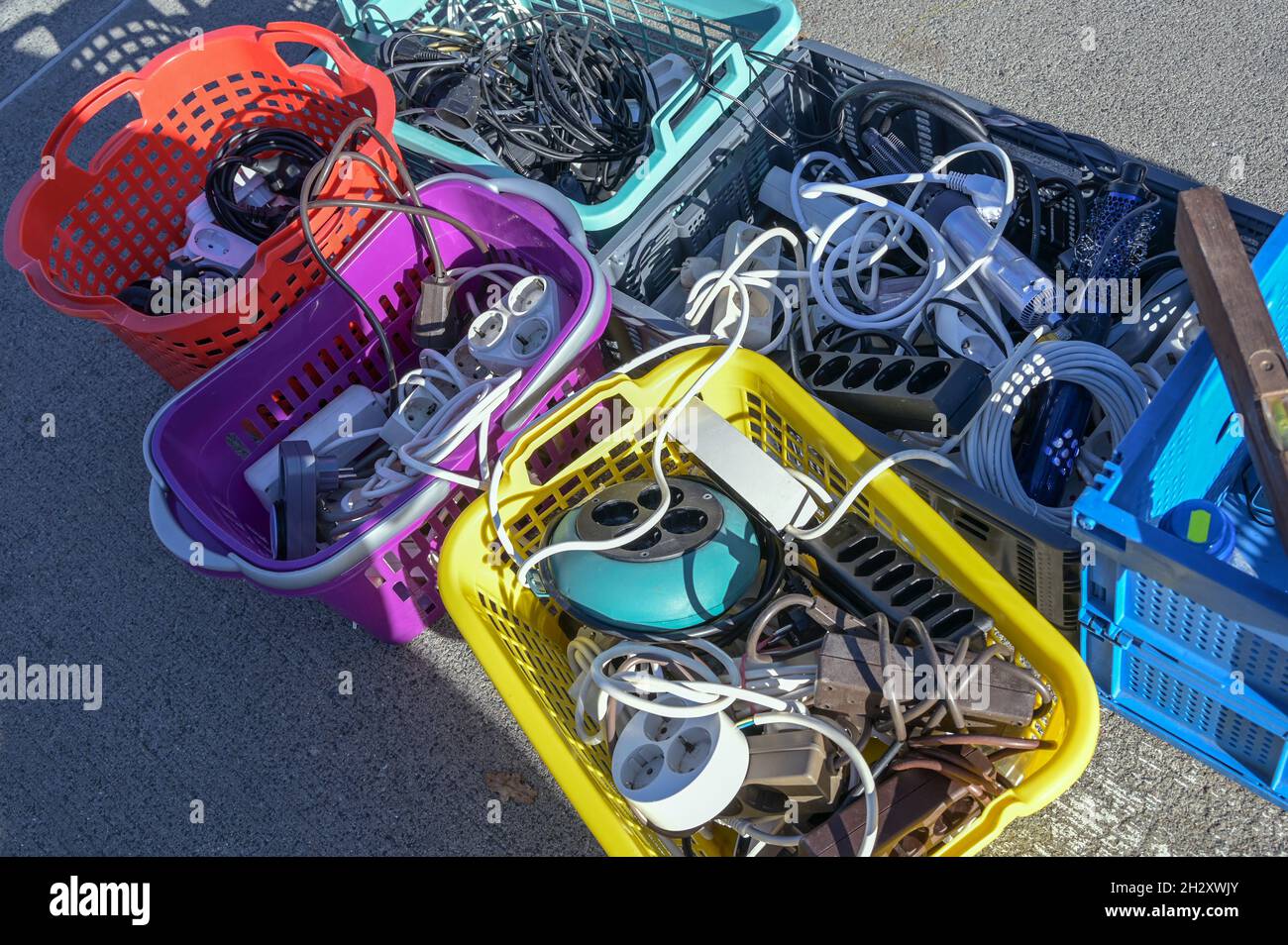 Gebrauchte Elektrokabel und Steckdosenleisten in bunten Kunststoffkörben auf der Straße auf einem Flohmarkt oder einem Garagenverkauf, ausgewählter Fokus, enge Fie-Tiefe Stockfoto