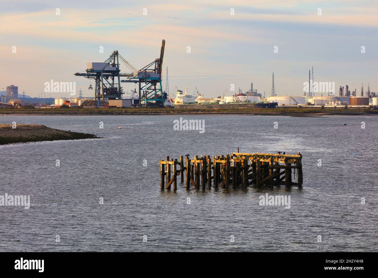 Eine alte hölzerne Landungsbrücke im Fluss Tees mit Kranen und einer Ölraffinerie im Hintergrund, Middlesbrough, North Yorkshire, England, Großbritannien. Stockfoto