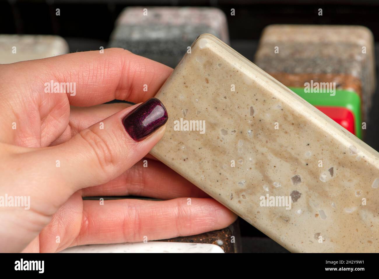 Eine Frau wählt Steinproben für eine Küchenarbeitsfläche aus. Ein Satz mehrfarbiger Proben aus künstlichem Acrylstein. Stockfoto