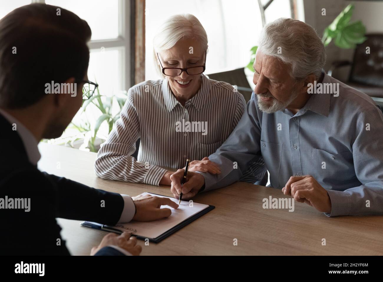 Glücklicher Ehemann Frau Rentner unterzeichnen Papierdokument bei der Versicherungsgesellschaft Stockfoto