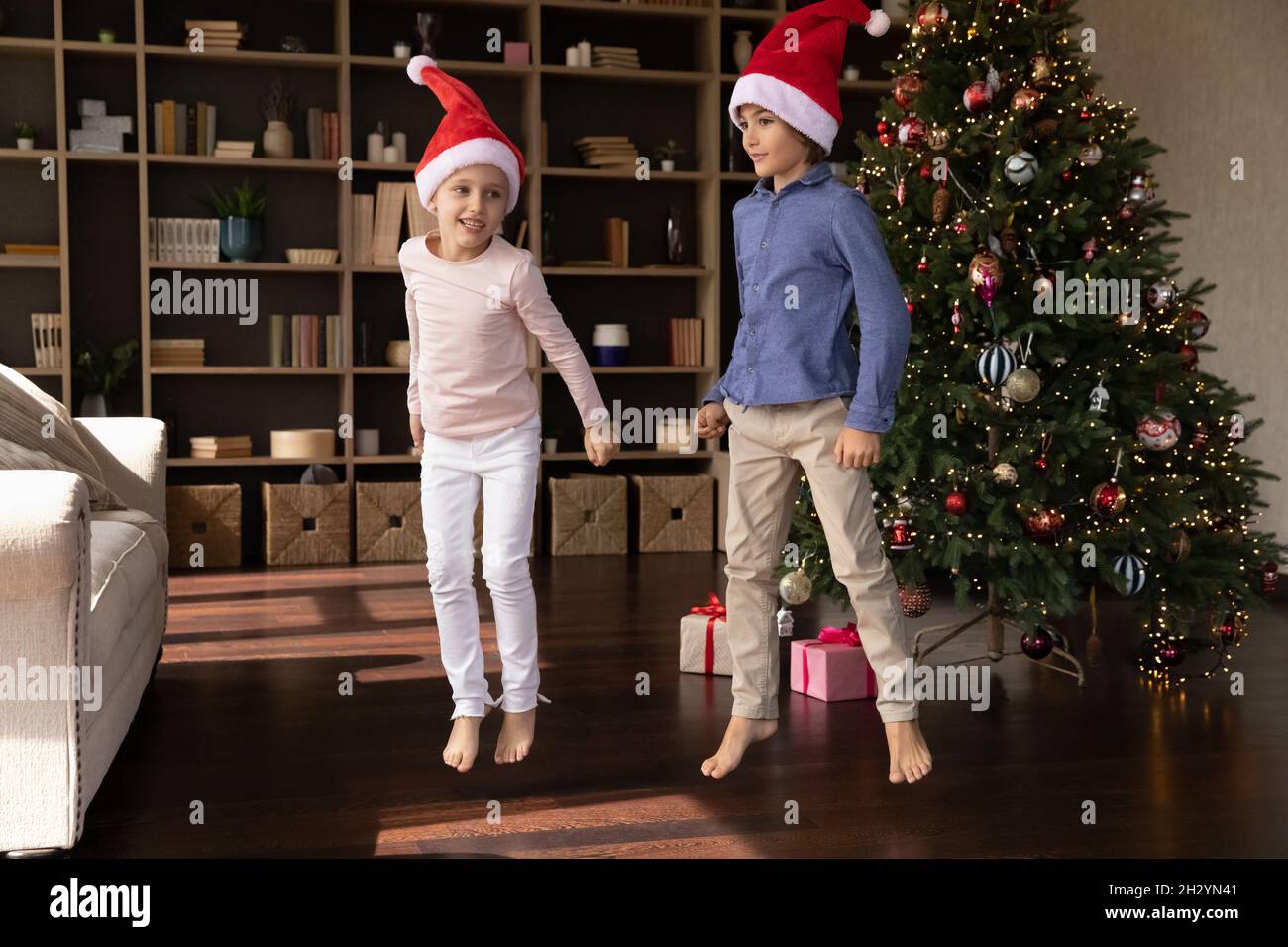 Glückliche kleine Kinder tanzen in der Nähe von Weihnachtsbaum. Stockfoto