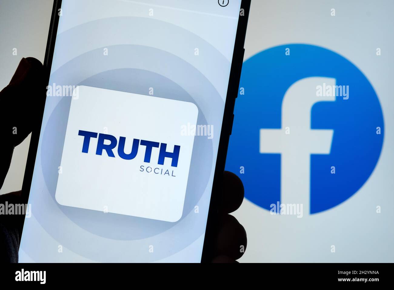 Das Logo der Truth Social App auf dem Smartphone mit verschwommenem Facebook-Logo auf dem Hintergrund. Neue Social-Media-Plattform von Donald Trump. Stafford, Einheit Stockfoto