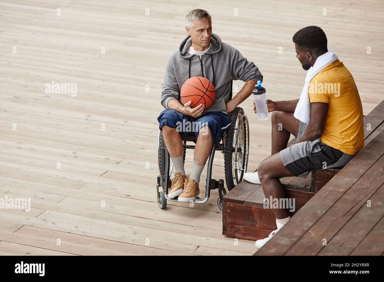 Reifer Mann mit Behinderung sitzt im Rollstuhl mit Ball und spricht mit afrikanischem Athleten über das Spiel Stockfoto