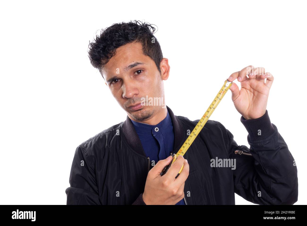 Mann mit Maßband, weißer Hintergrund. Junger Latino-Mann, der zeigt, wie man ein Maßband verwendet. Stockfoto