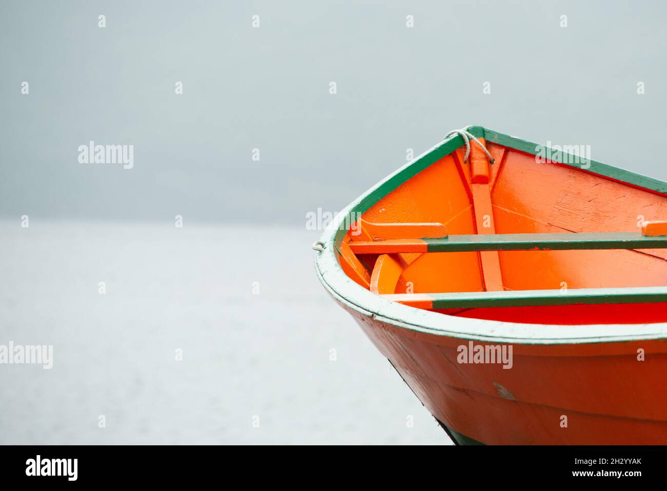 Ein helles, farbenfrohes, orangefarbenes und grünes Holzfischerboot, Holzboot, auf der Bucht. Es gibt Nebel, Regen und Nebel im Hintergrund. Die Szene ist düster. Stockfoto
