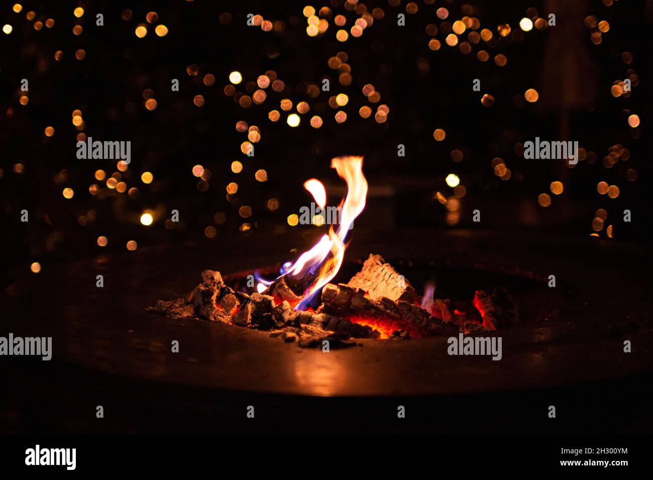 Nahaufnahme des Kamins mit brennendem Kaminholz in der kalten Winternacht und Bokeh weihnachtslichter auf dem traditionellen weihnachtsmarkt in Meran, Südtirol Stockfoto