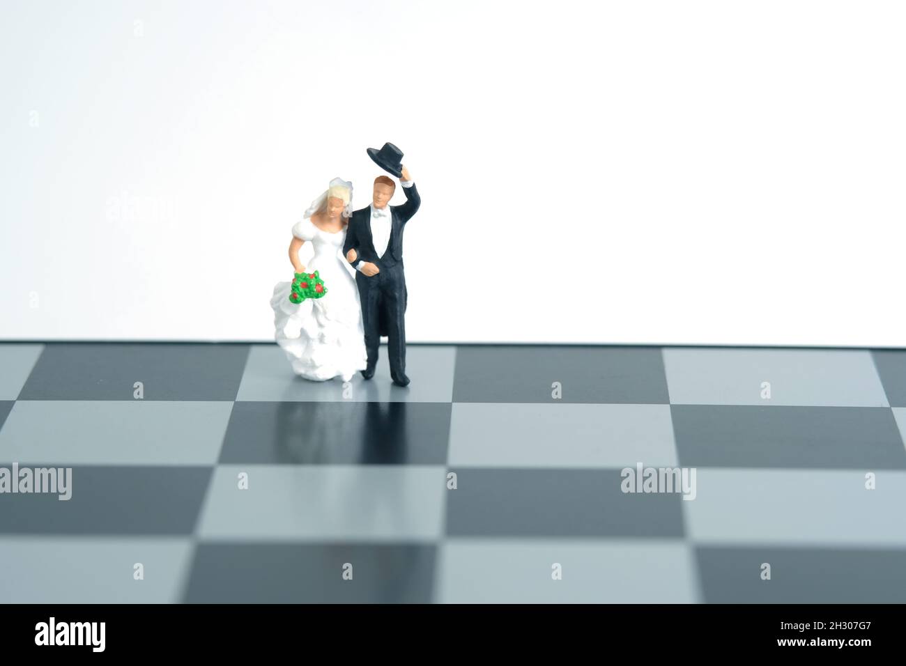 Hochzeit Ehe Strategie Plan Konzept Miniatur Menschen, Spielzeug Fotografie. Braut und Bräutigam stehen über Schachbrett isoliert auf weißem Hintergrund. Ima Stockfoto