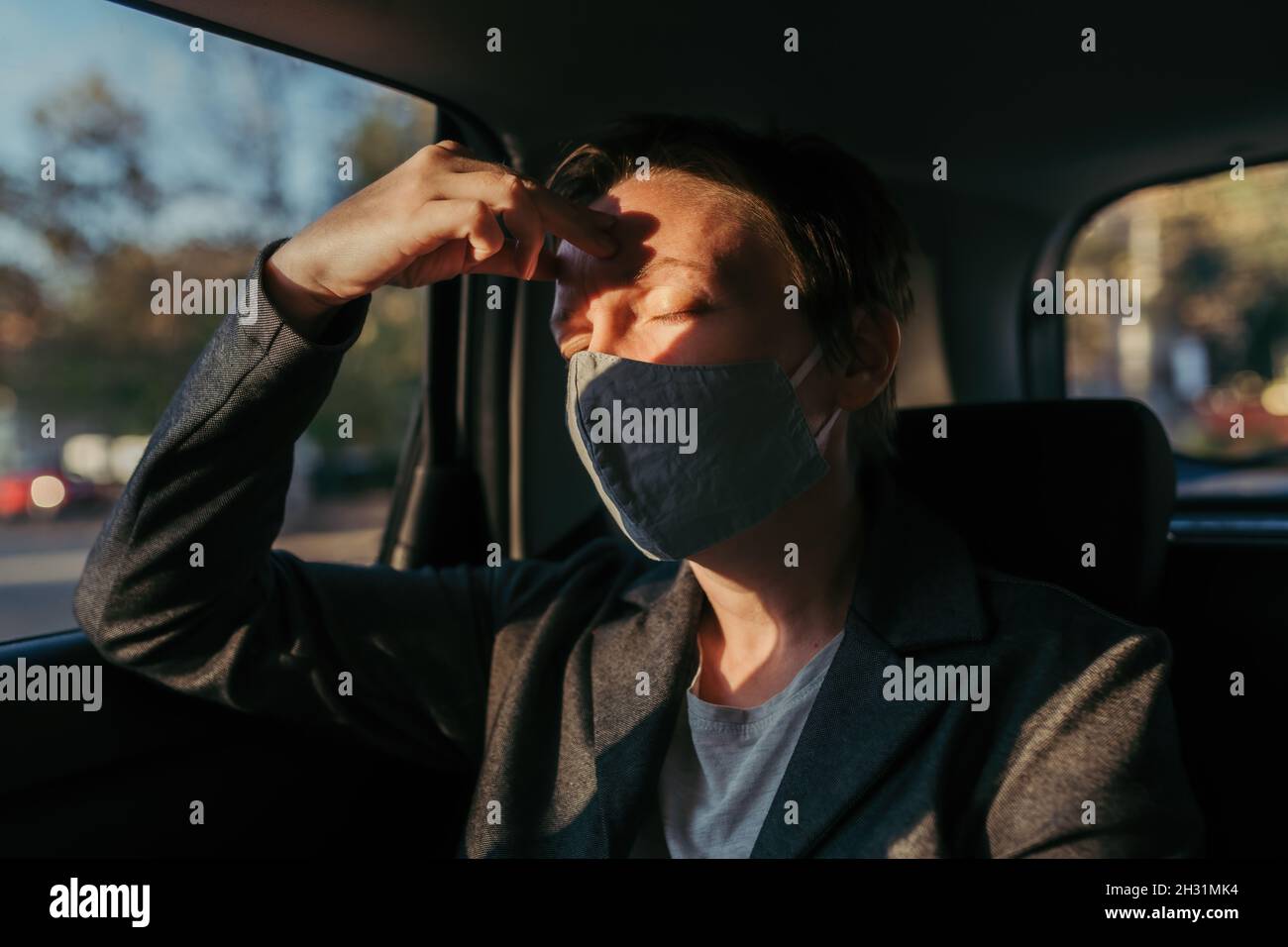 Geschäftsfrau mit starken Kopfschmerzen Schmerzsymptomen und schützender Gesichtsmaske auf dem Rücksitz eines Autos, selektiver Fokus Stockfoto