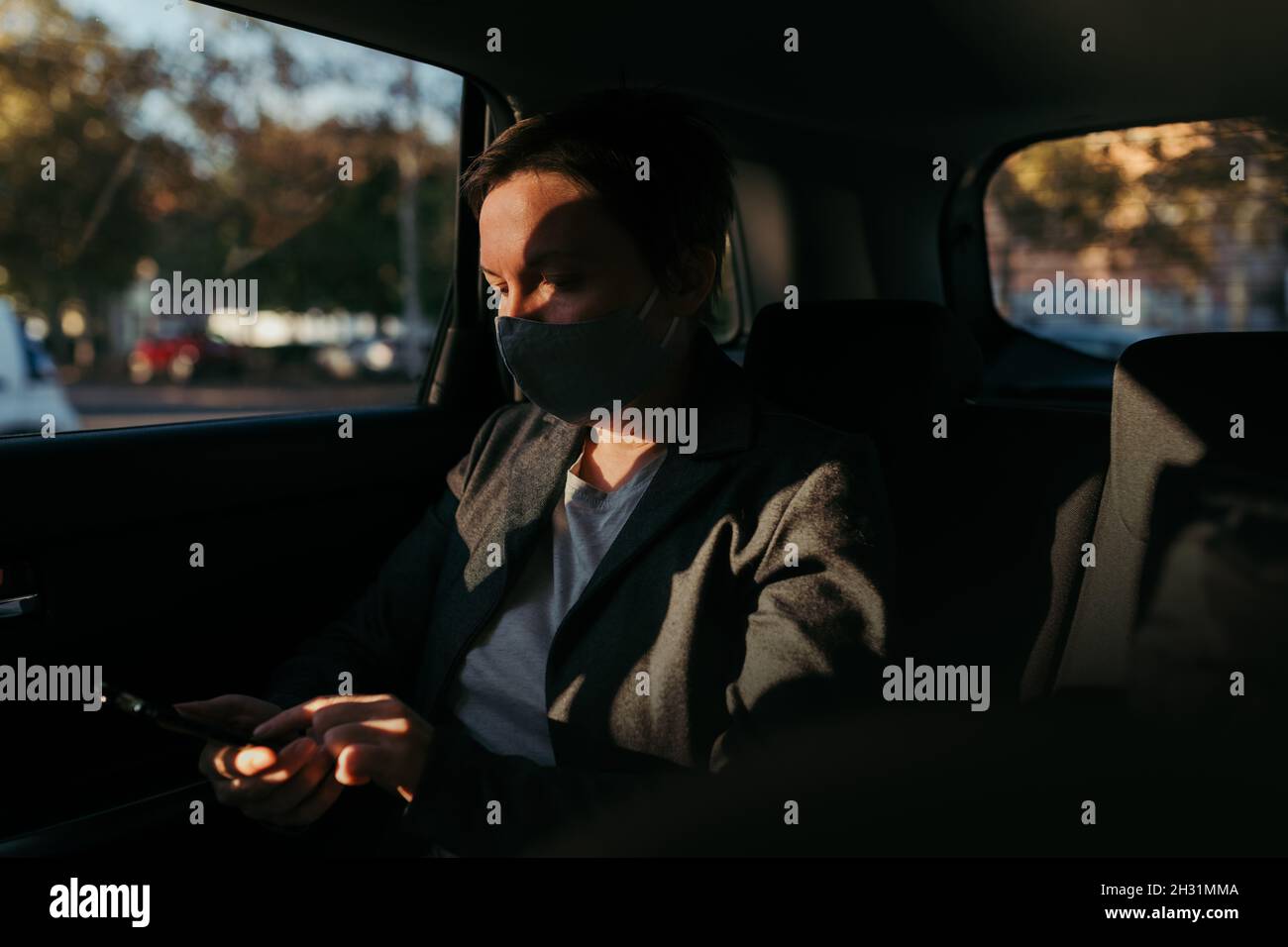 Geschäftsfrau, die im Auto eine Textnachricht tippt, während sie eine schützende Gesichtsmaske für eine Covid-19-Pandemie trägt, selektiver Fokus Stockfoto