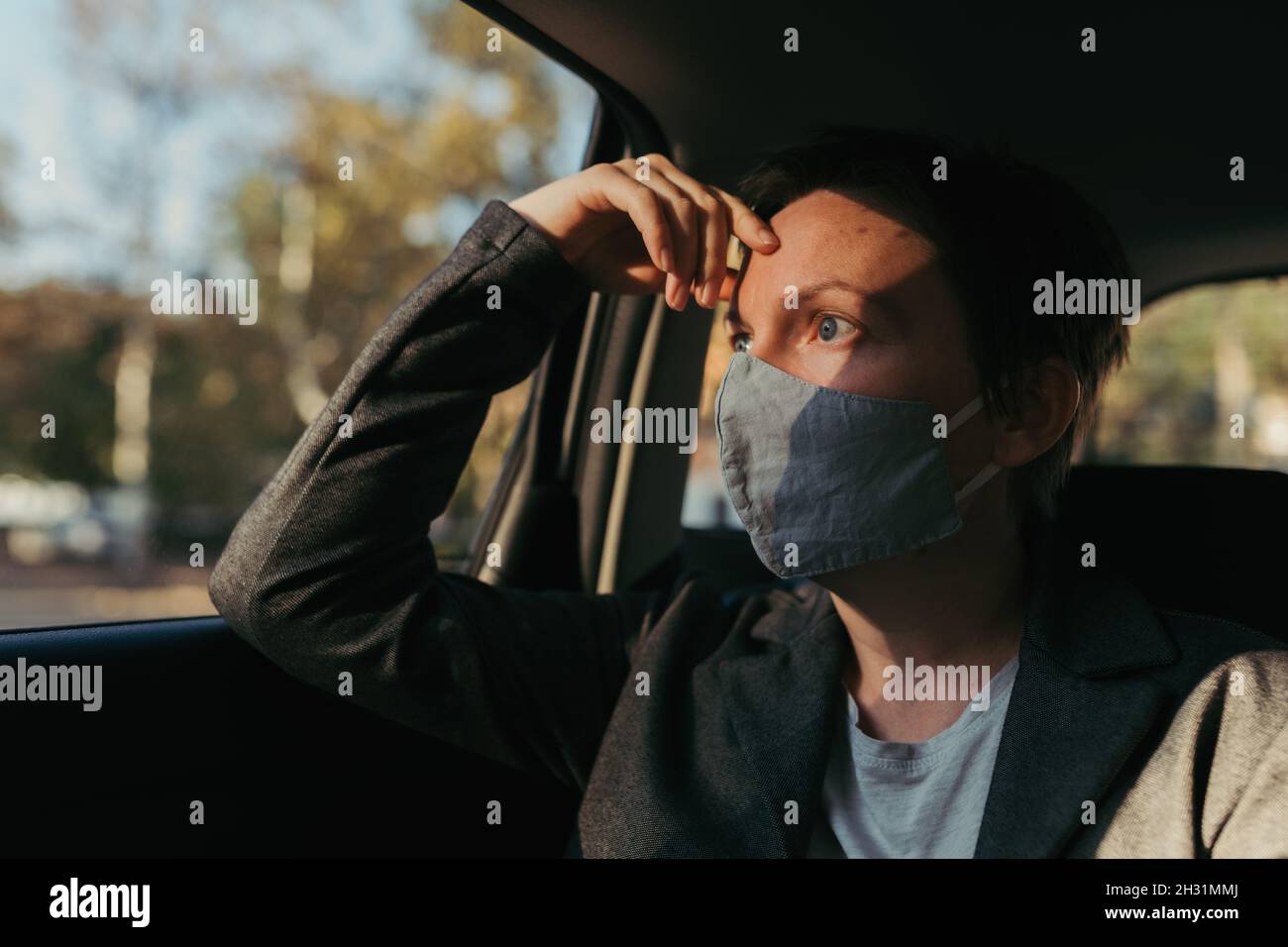 Besorgte Geschäftsfrau mit schützender Gesichtsmaske wartet im Auto und schaut aus dem Fenster, selektive Fokus Stockfoto