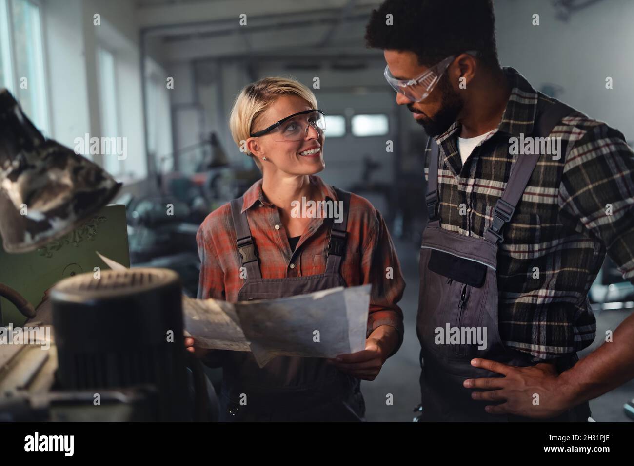 Porträt junger birazialer Industriekollegen, die in Innenräumen in einer Metallwerkstatt arbeiten, lächelnd. Stockfoto