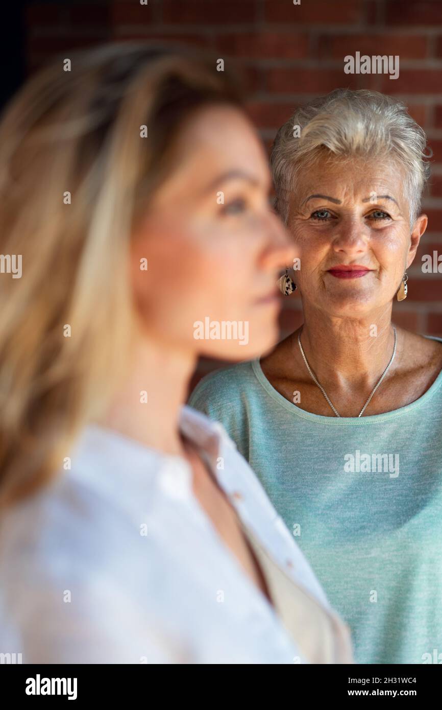 Ältere Mutter, die ihre Erwachsene Tochter zuhause ansieht. Selektiver Fokus auf Frau im Hintergrund. Stockfoto