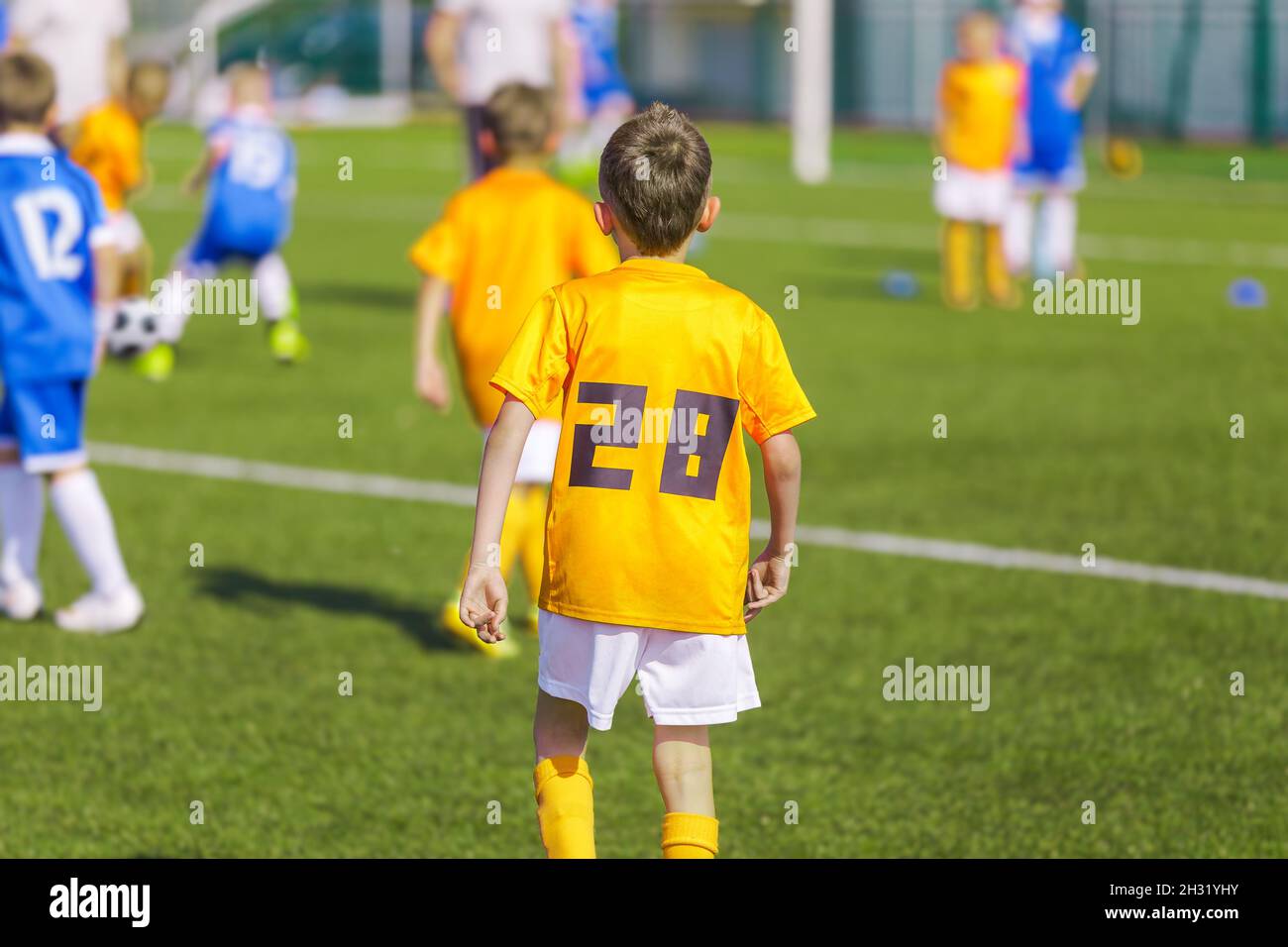 Kinder in Fußball-Trikot-Uniformen spielen Junior League Spiel. Happy Boys kicking Ball on Grass Venue. Zwei Kinder-Fußballmannschaften in Gelb- und Blauer Shir Stockfoto