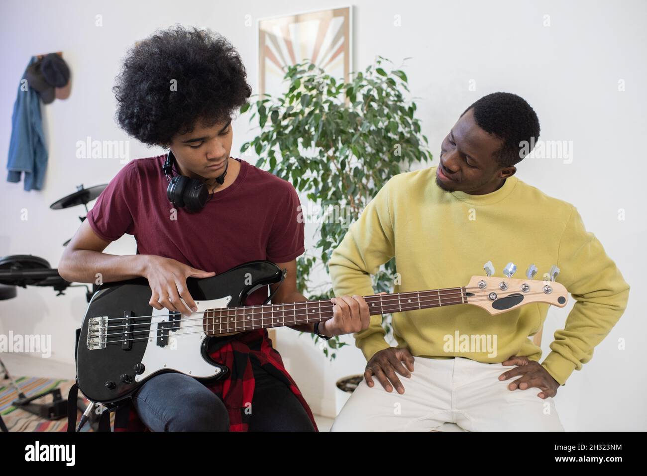Teenager spielt Gitarre, während sein Lehrer in der Nähe sitzt und ihn zu Hause beim Unterricht konsultiert Stockfoto