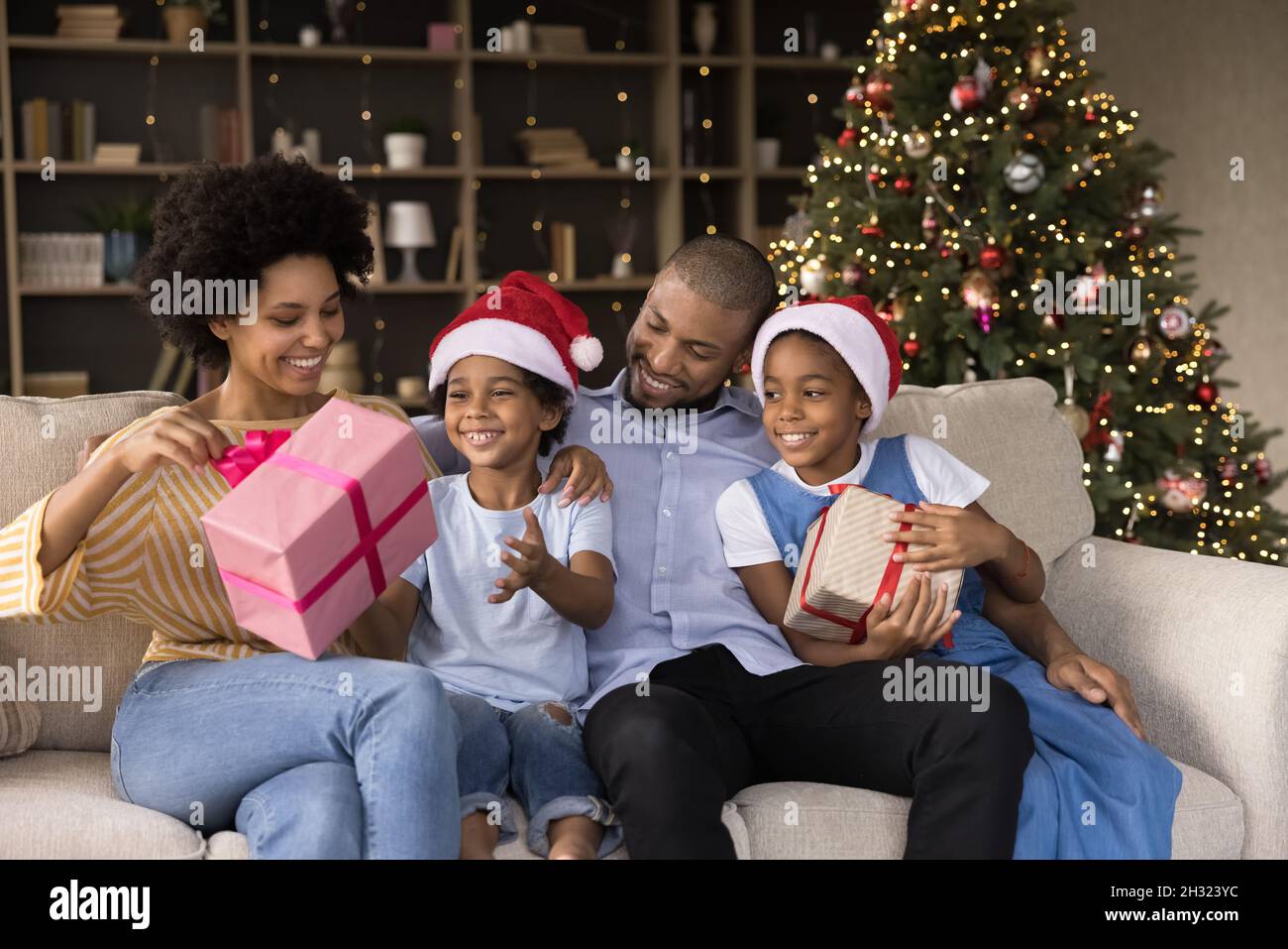 Lächelnde junge afroamerikanische Eltern packen Geschenke mit Kindern aus. Stockfoto