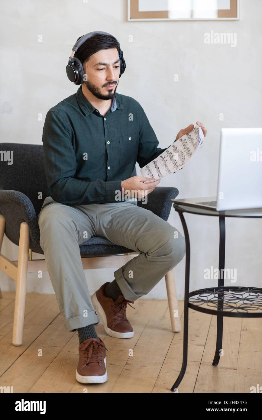 Junge Musiklehrerin mit Kopfhörern, die den Schülern während des Online-Unterrichts Notizen auf dem Laptop-Bildschirm zeigt Stockfoto