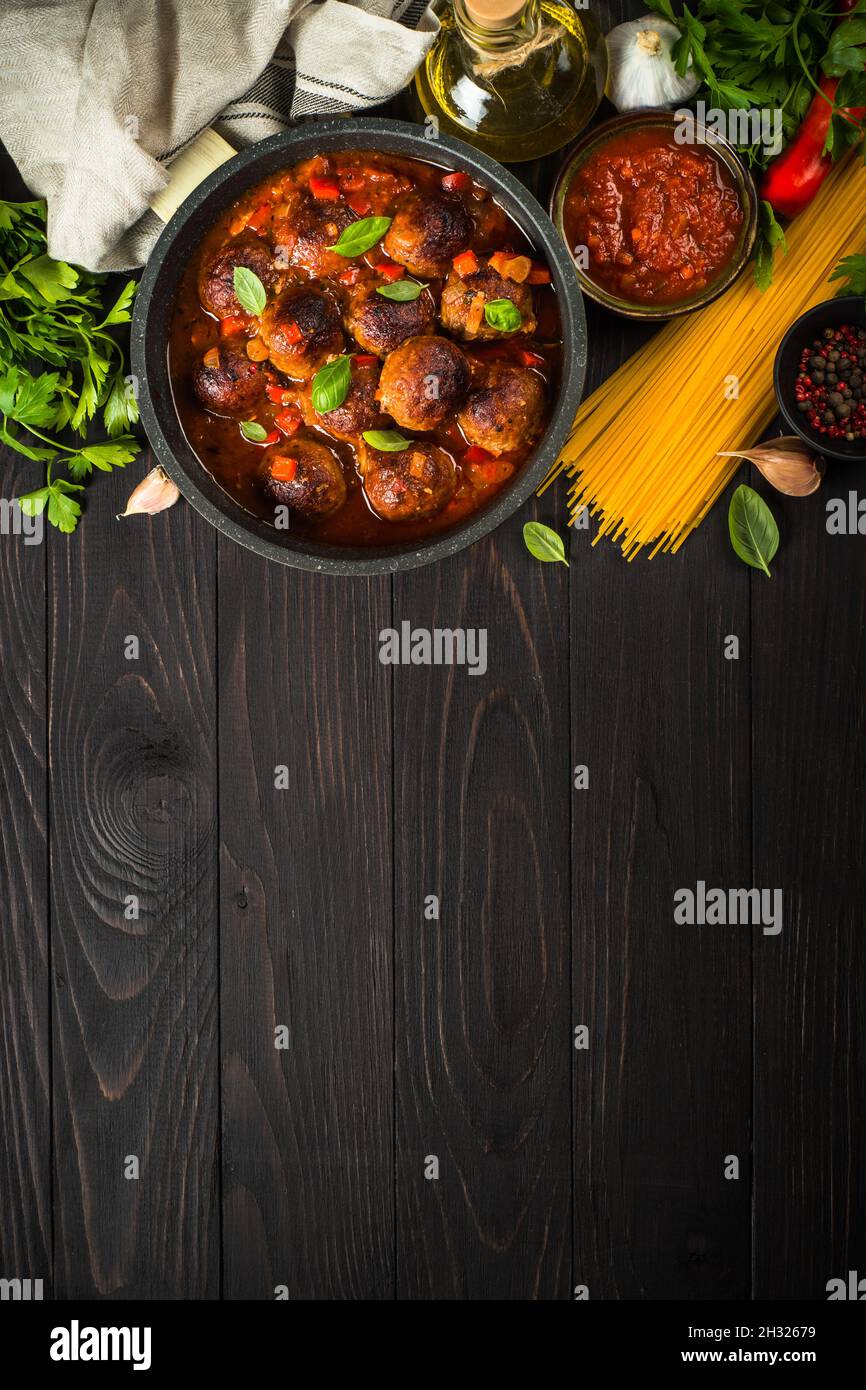 Fleischbällchen in Tomatensauce und Pasta auf dunklem Holztisch. Stockfoto