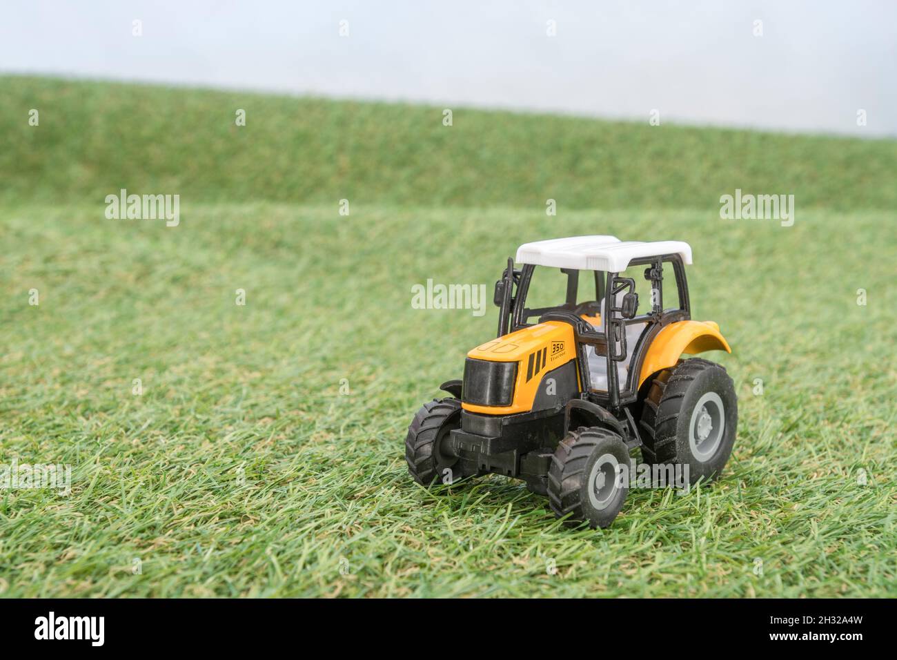 Kleiner Spielzeugtraktor, der auf einem „Feld“ aus faux/fake Gras steht. Für die britische Lebensmittelproduktion, Farm-to-Fork, Field-to-Fork/Field-to-Plate und die britische Landwirtschaft. Stockfoto