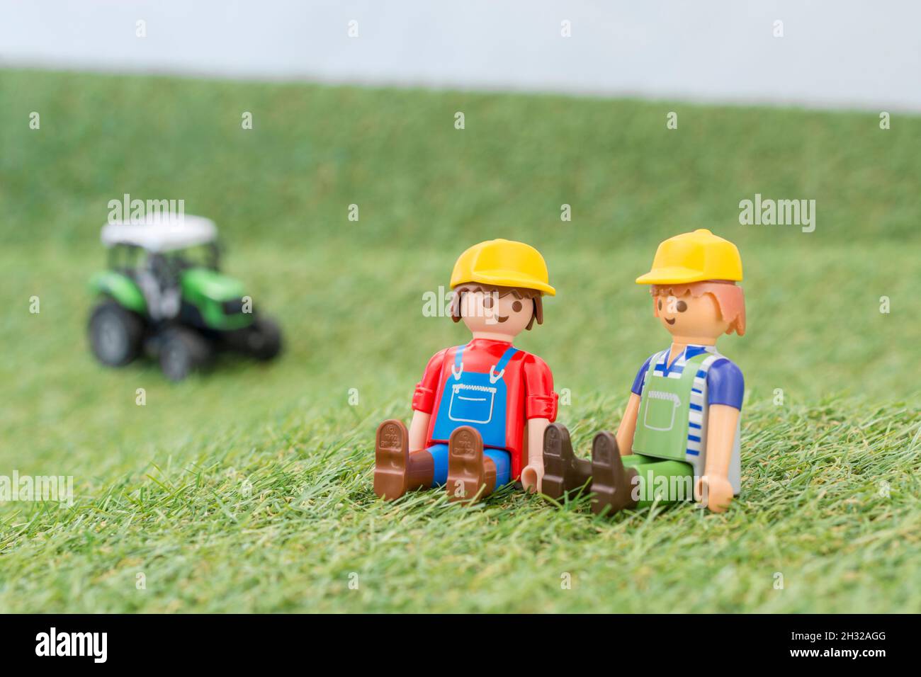 Kleiner Spielzeugtraktor auf faux / gefälschtem Gras mit Spielzeug Playmobil Landwirt Figur. Für die britische Lebensmittelproduktion: Farm to Fork, Field to Fork / Field to Plate Stockfoto