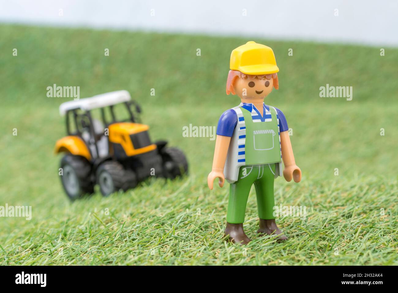 Kleiner Spielzeugtraktor auf faux / gefälschtem Gras mit Spielzeug Playmobil Landwirt Figur. Für die britische Lebensmittelproduktion: Farm to Fork, Field to Fork / Field to Plate Stockfoto