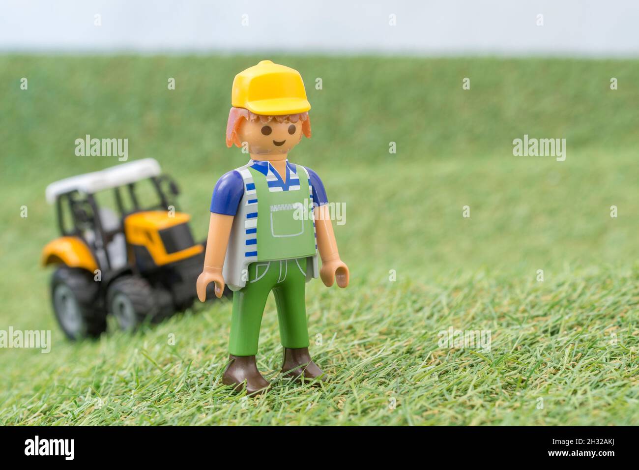 Kleiner Spielzeugtraktor auf faux / gefälschtem Gras mit Spielzeug Playmobil Landwirt Figur. Für die britische Lebensmittelproduktion: Farm to Fork, Field to Fork / Field to Plate Stockfoto
