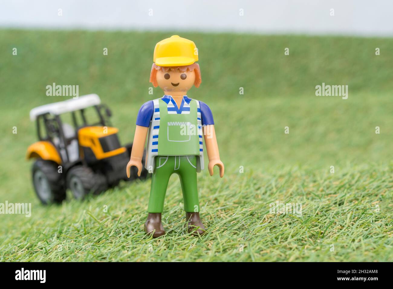 Kleiner Spielzeugtraktor auf faux / gefälschtem Gras mit Spielzeug Playmobil Landwirt Figur. Für die britische Lebensmittelproduktion: Farm to Fork, Field to Fork / Field to Plate Stockfoto