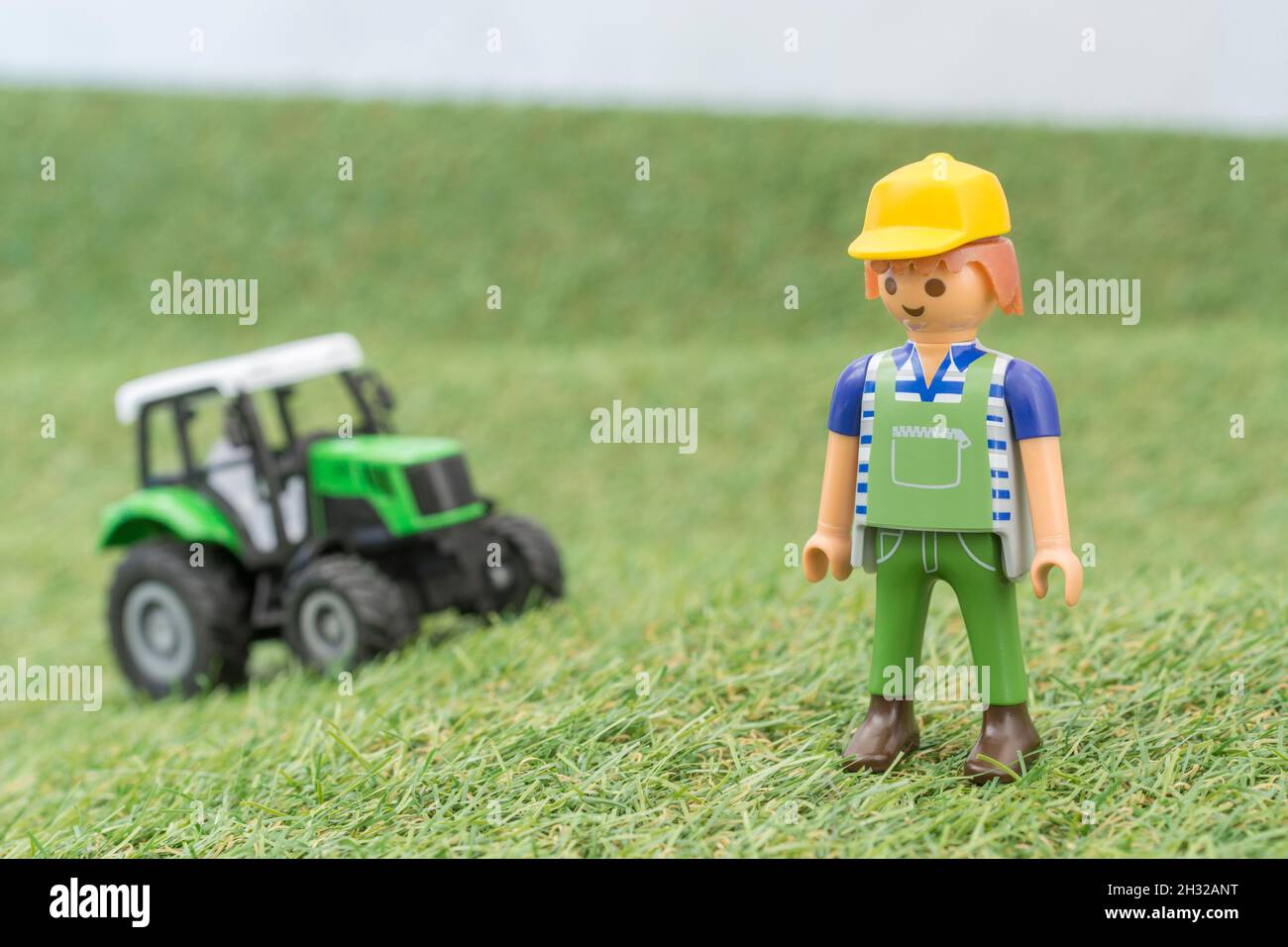 Kleiner Spielzeugtraktor auf faux / gefälschtem Gras mit Spielzeug Playmobil Landwirt Figur. Für die britische Lebensmittelproduktion: Farm to Fork, Field to Fork / Field to Plate Stockfoto