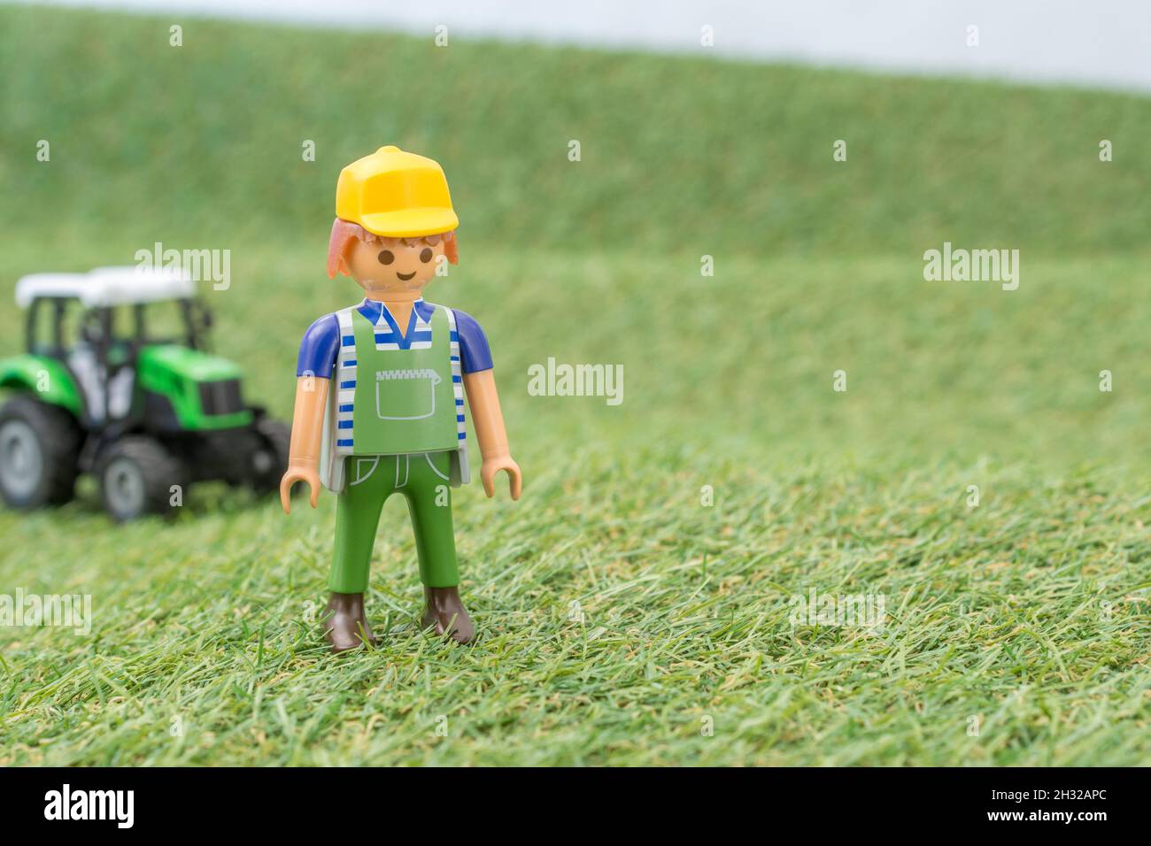 Kleiner Spielzeugtraktor auf faux / gefälschtem Gras mit Spielzeug Playmobil Landwirt Figur. Für die britische Lebensmittelproduktion: Farm to Fork, Field to Fork / Field to Plate Stockfoto