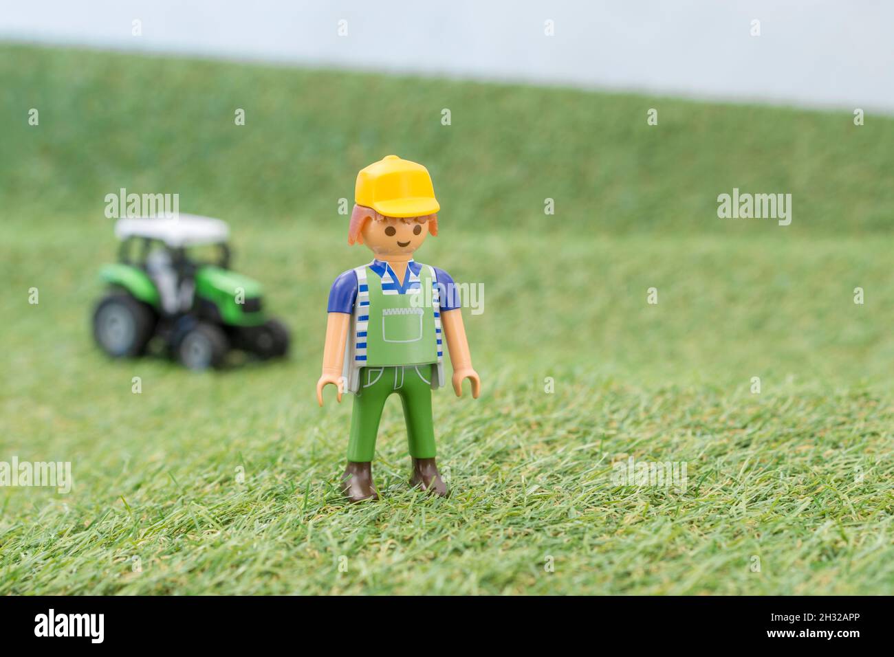 Kleiner Spielzeugtraktor auf faux / gefälschtem Gras mit Spielzeug Playmobil Landwirt Figur. Für die britische Lebensmittelproduktion: Farm to Fork, Field to Fork / Field to Plate Stockfoto