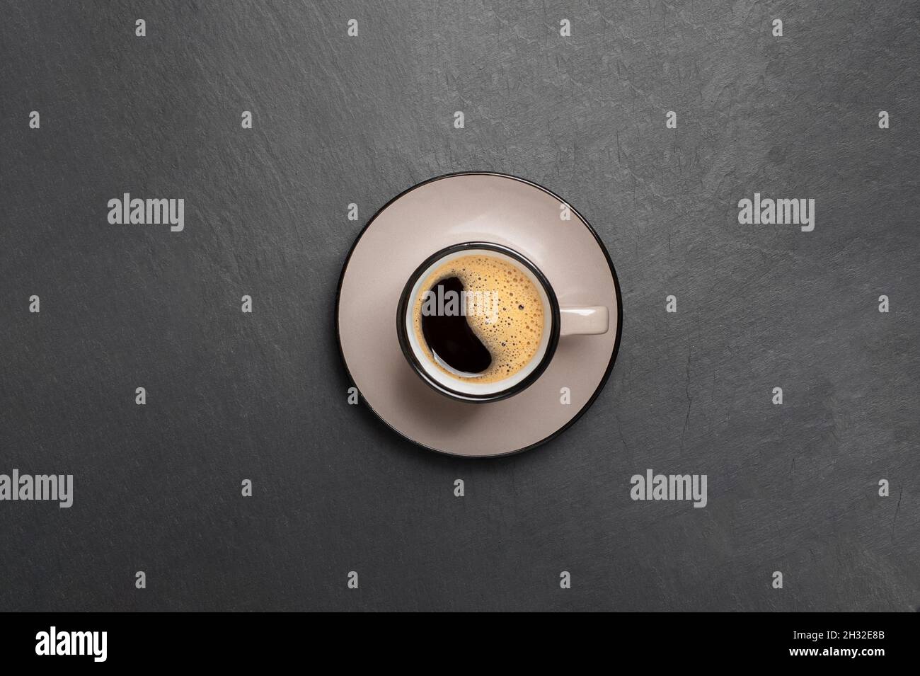 Eine Tasse Kaffee mit schönem Schaum in der Nähe Kaffeebohnen sind auf einem schwarzen Stein Hintergrund Draufsicht Kopierfläche verstreut Stockfoto