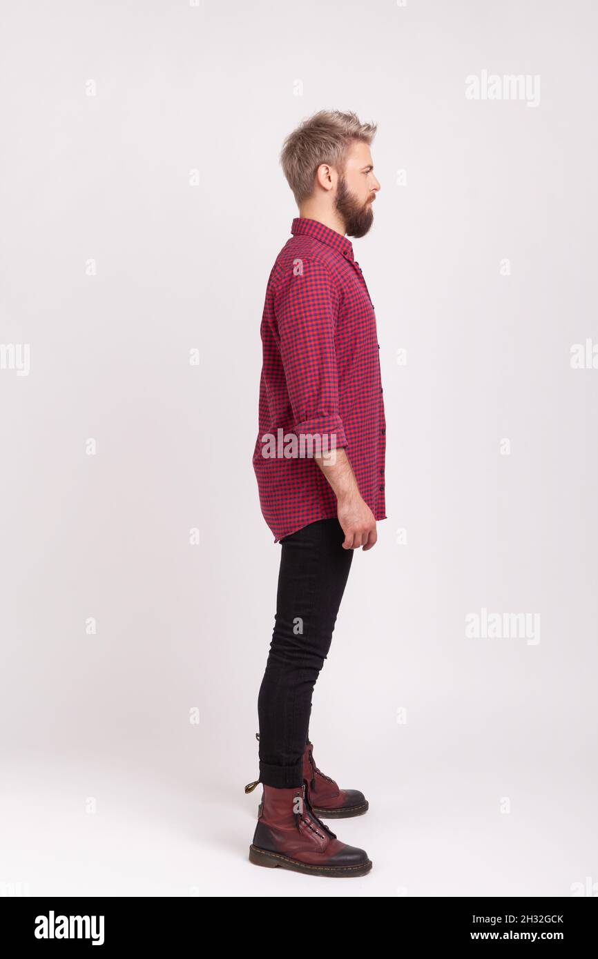 Seitenansicht Ganzkörperlänge von ernst selbstbewussten bärtigen Mann trägt rote karierte Hemd und lässige schwarze Hosen posiert, üben Modellierung. Innenaufnahme des Studios isoliert auf grauem Hintergrund Stockfoto