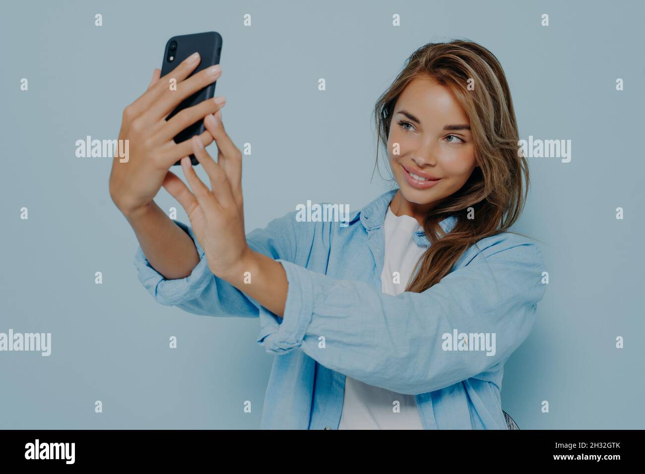 Attraktive Bloggerin, die Selfie in der Nähe einer hellblauen Wand macht Stockfoto
