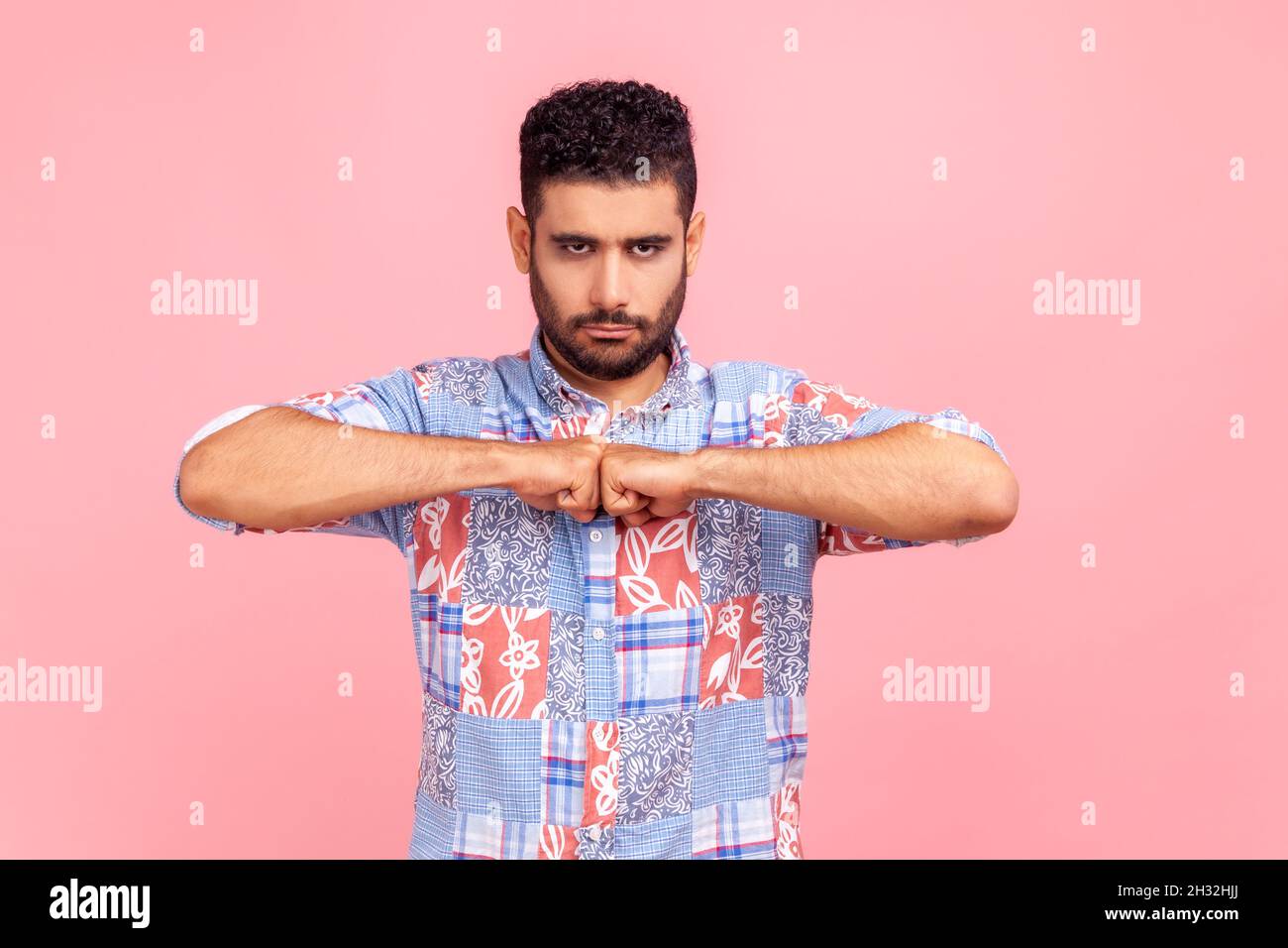 Junger, aggressiver bärtiger Mann, der die Fäuste zusammenhält, bereit ist zu kämpfen, Wut ausdrückt, negative Emotionen hat. Innenaufnahme des Studios isoliert auf rosa Hintergrund. Stockfoto